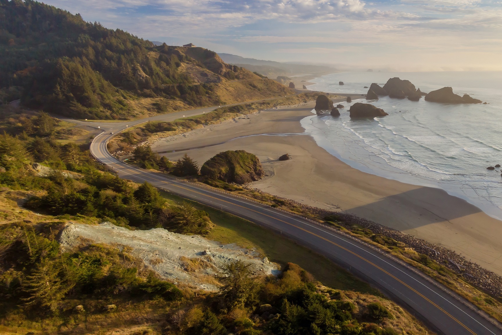 Scenic coastal highway winding along rugged cliffs with ocean waves and sea stacks below